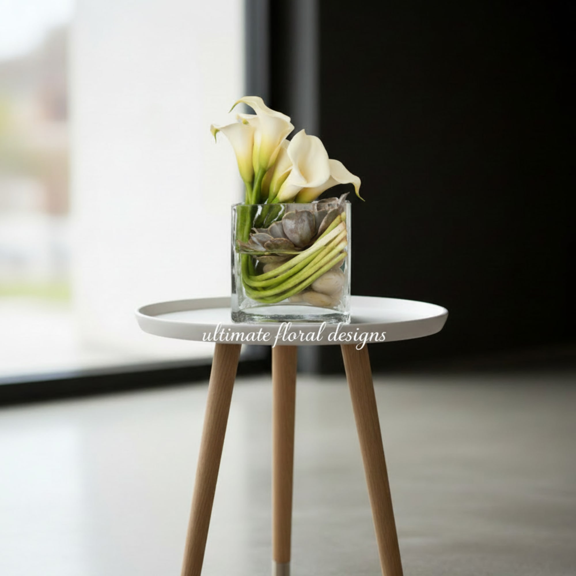 White calla lilies in a clear glass vase with succulents