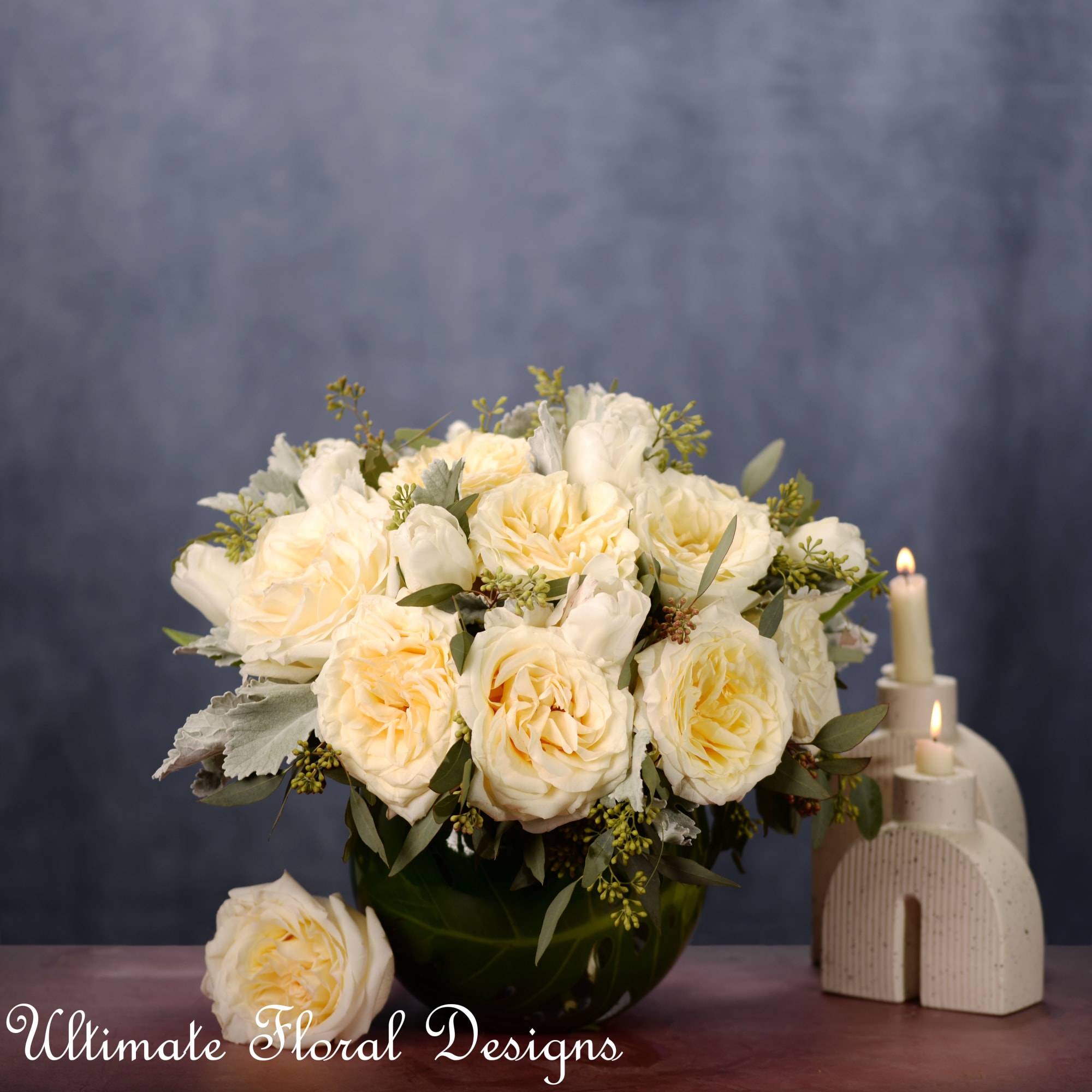 Cream rose bouquet in a dark vase beside lit candles