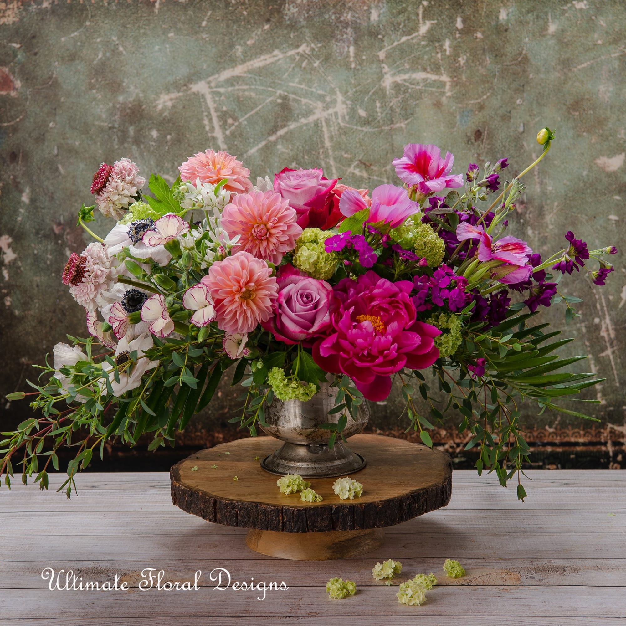 Colorful mixed flower arrangement in a silver vase on a wood slab