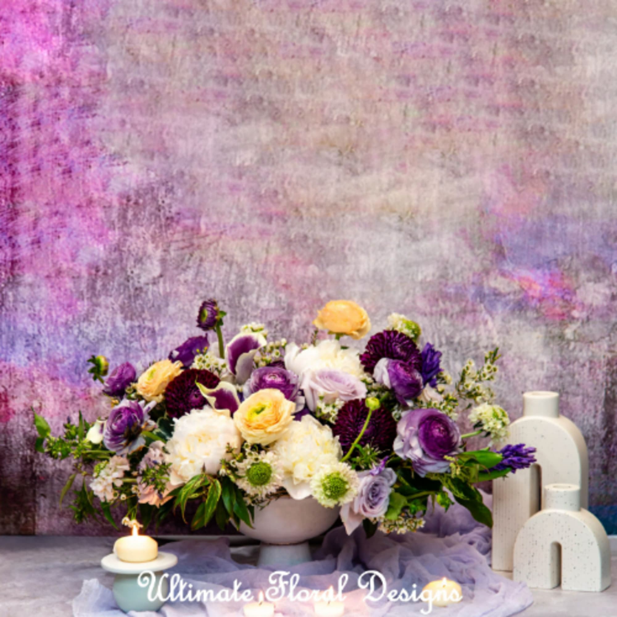 Low floral arrangement of purple, white, and peach blooms in a white vase