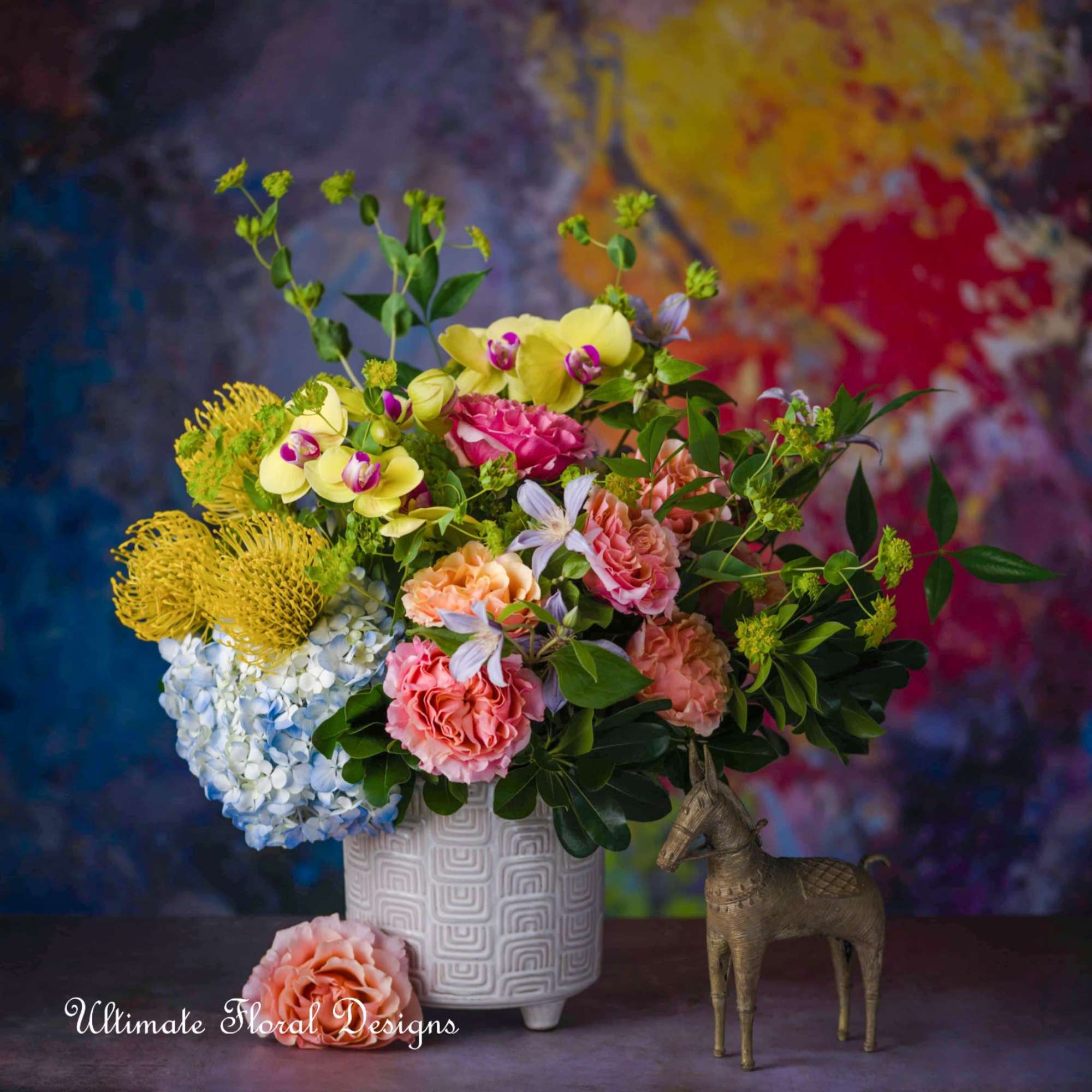 Colorful mixed flower arrangement in a white textured vase with a small horse figurine