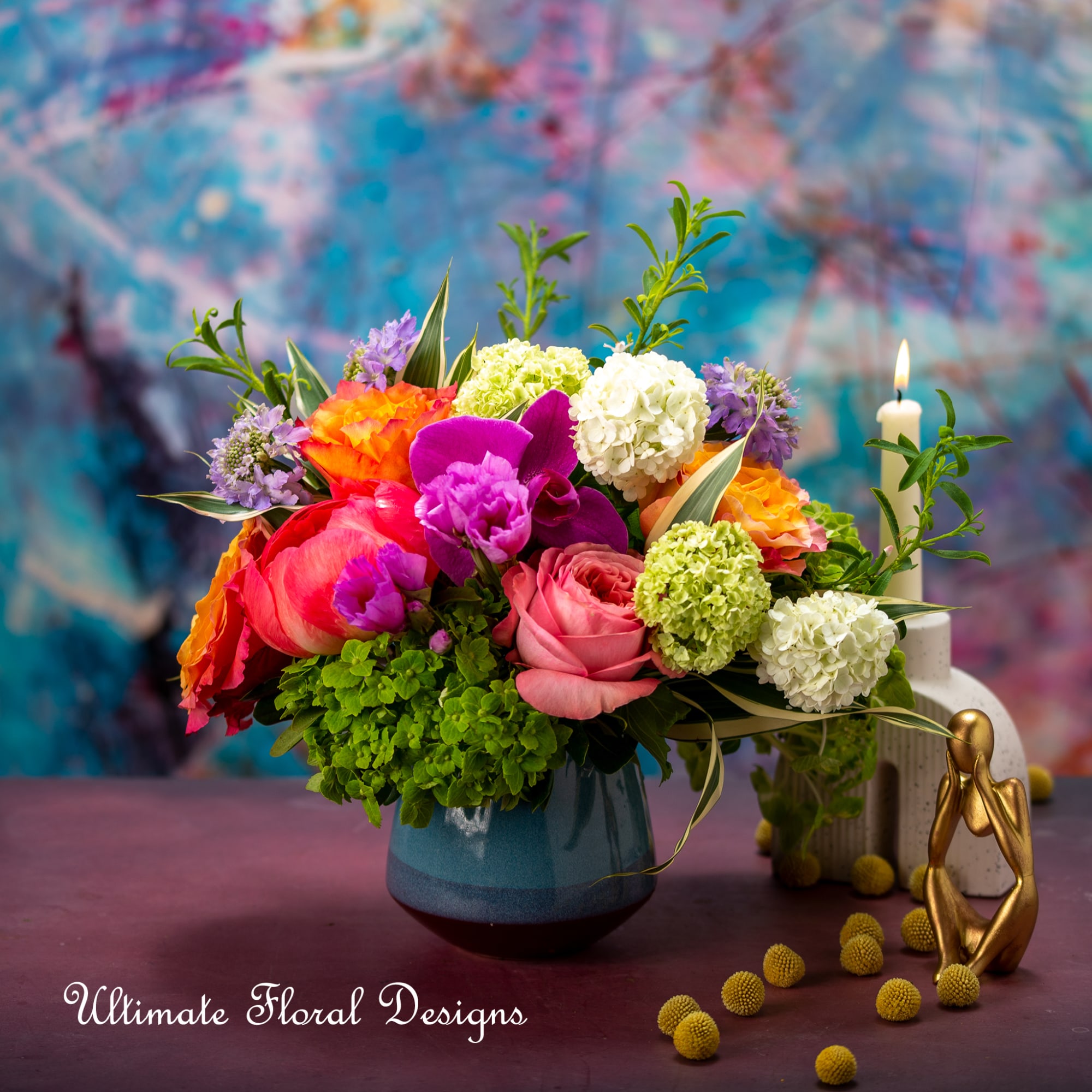 Colorful mixed flower arrangement in a blue vase beside a lit candle