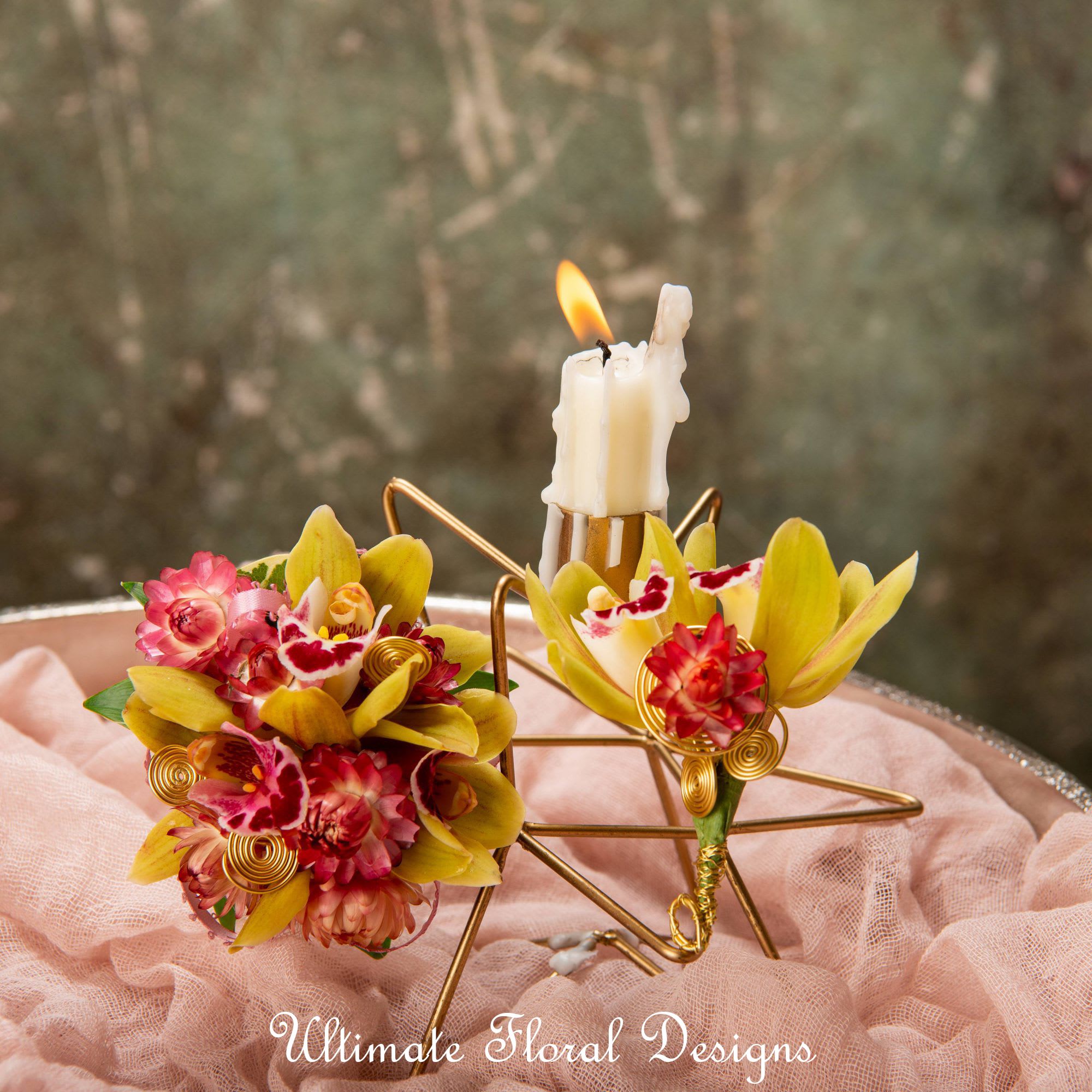 Two small floral arrangements with a lit candle on a gold star stand