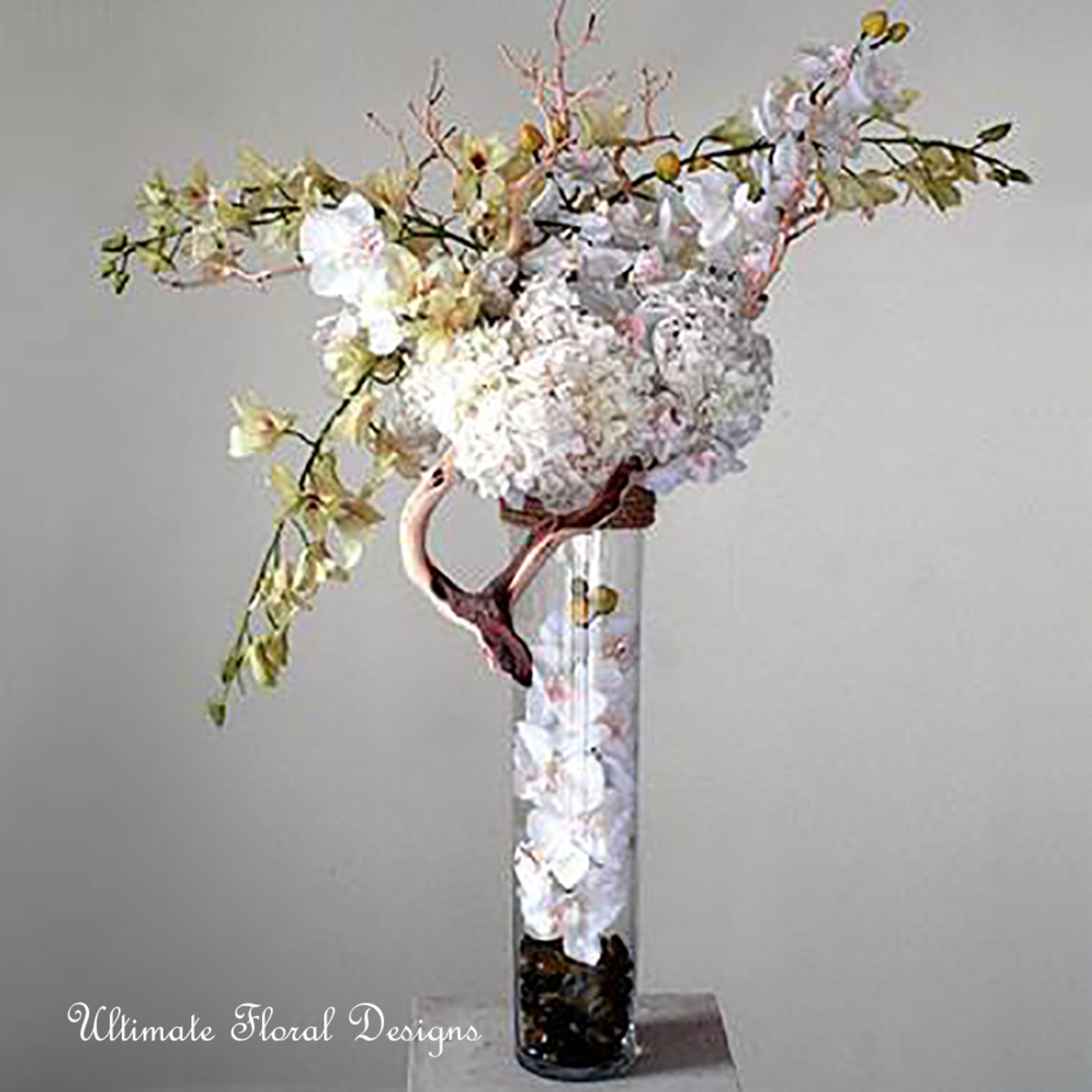 Tall white floral arrangement in a clear glass vase with arching branches