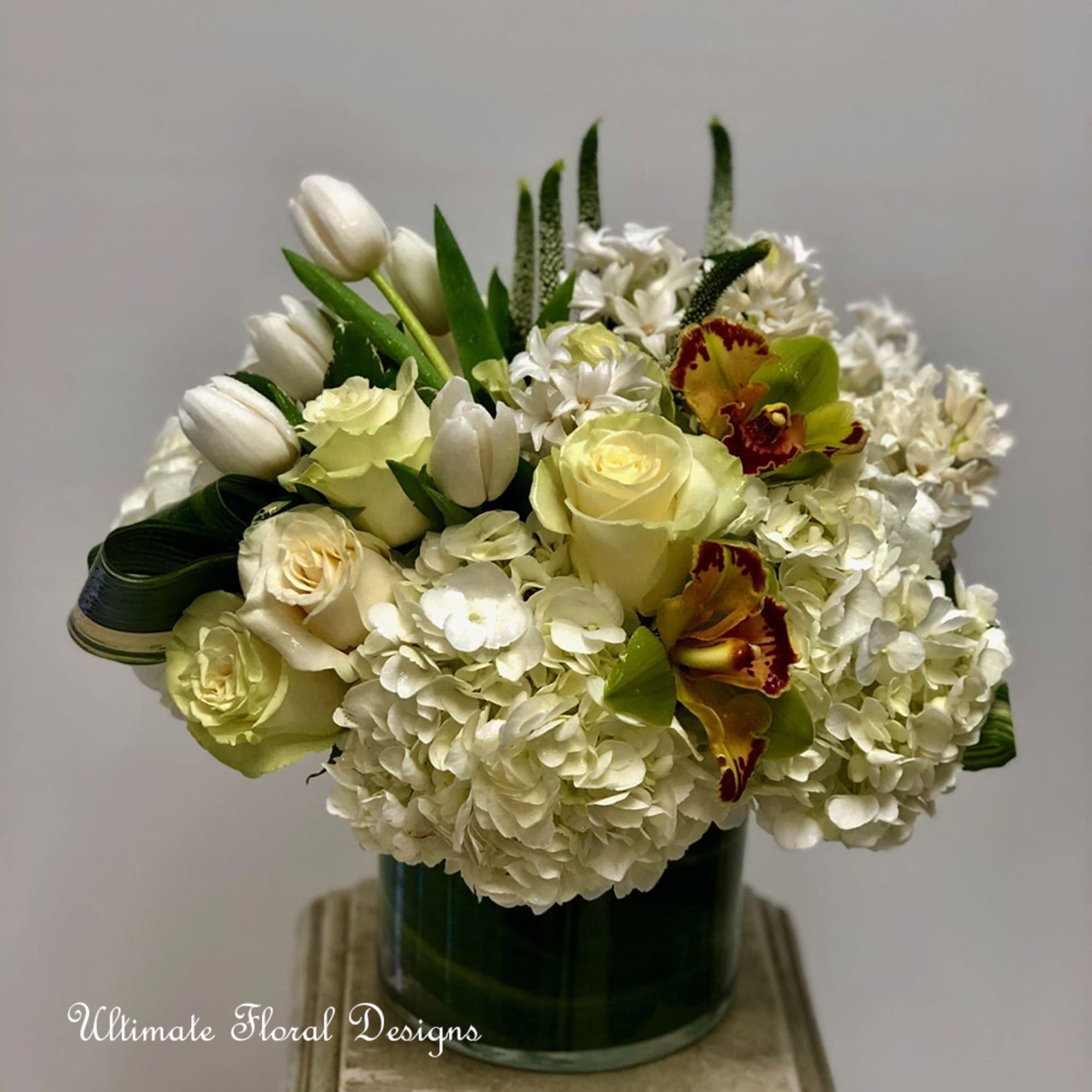 White floral arrangement in a dark green vase with tulips, roses, and orchids