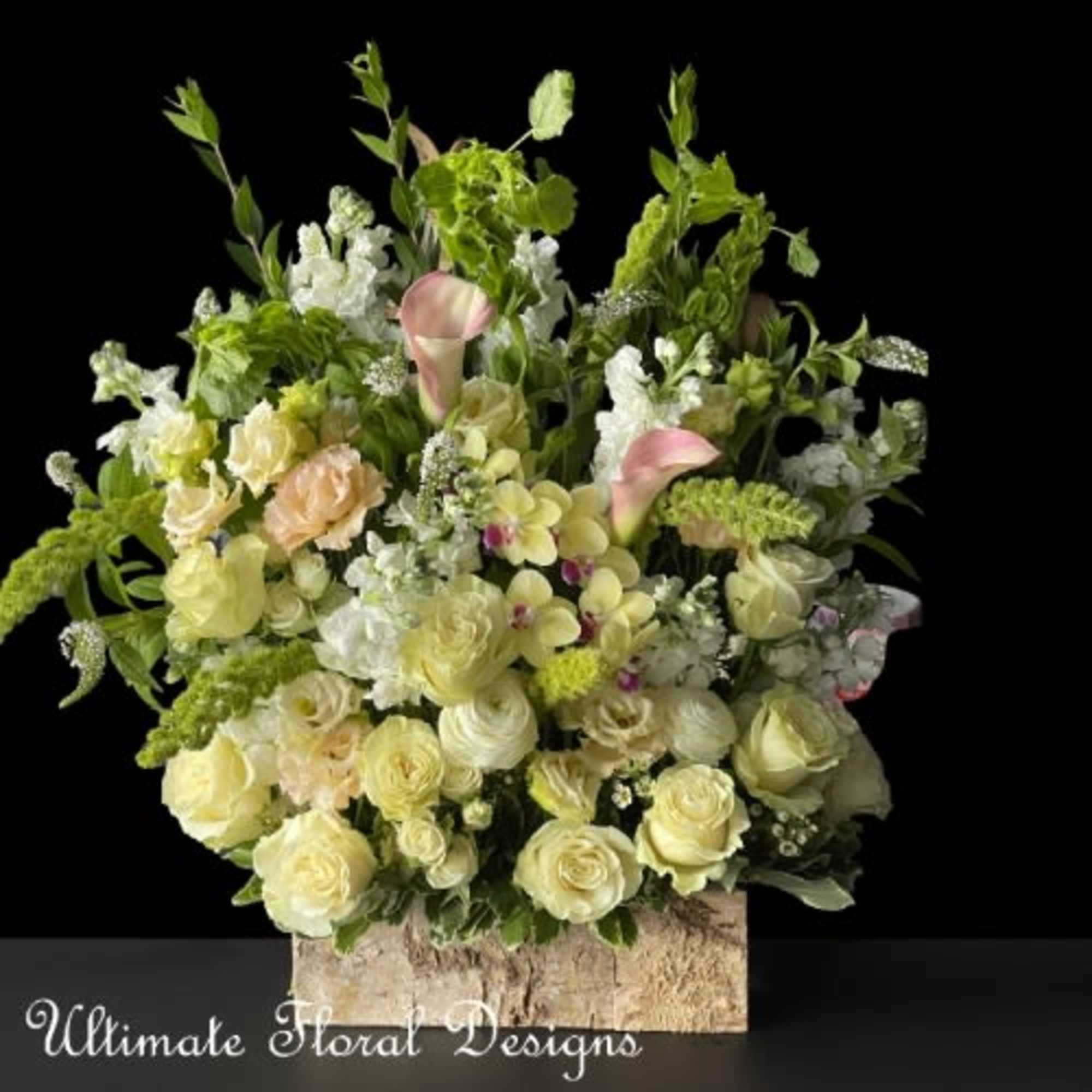 Large floral arrangement with pale roses, calla lilies, and green accents in a rustic container