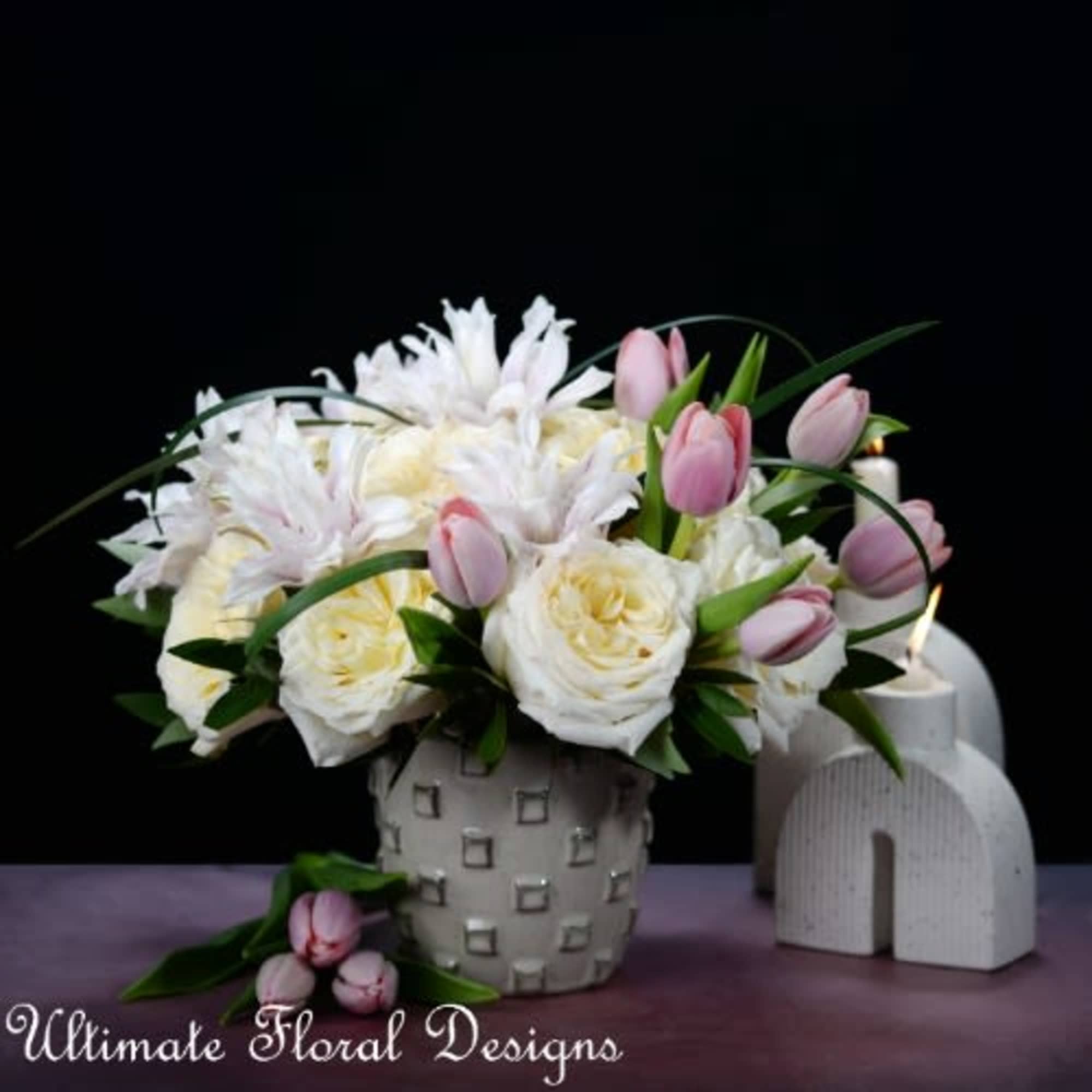 White and pink floral arrangement in a patterned vase with candles nearby