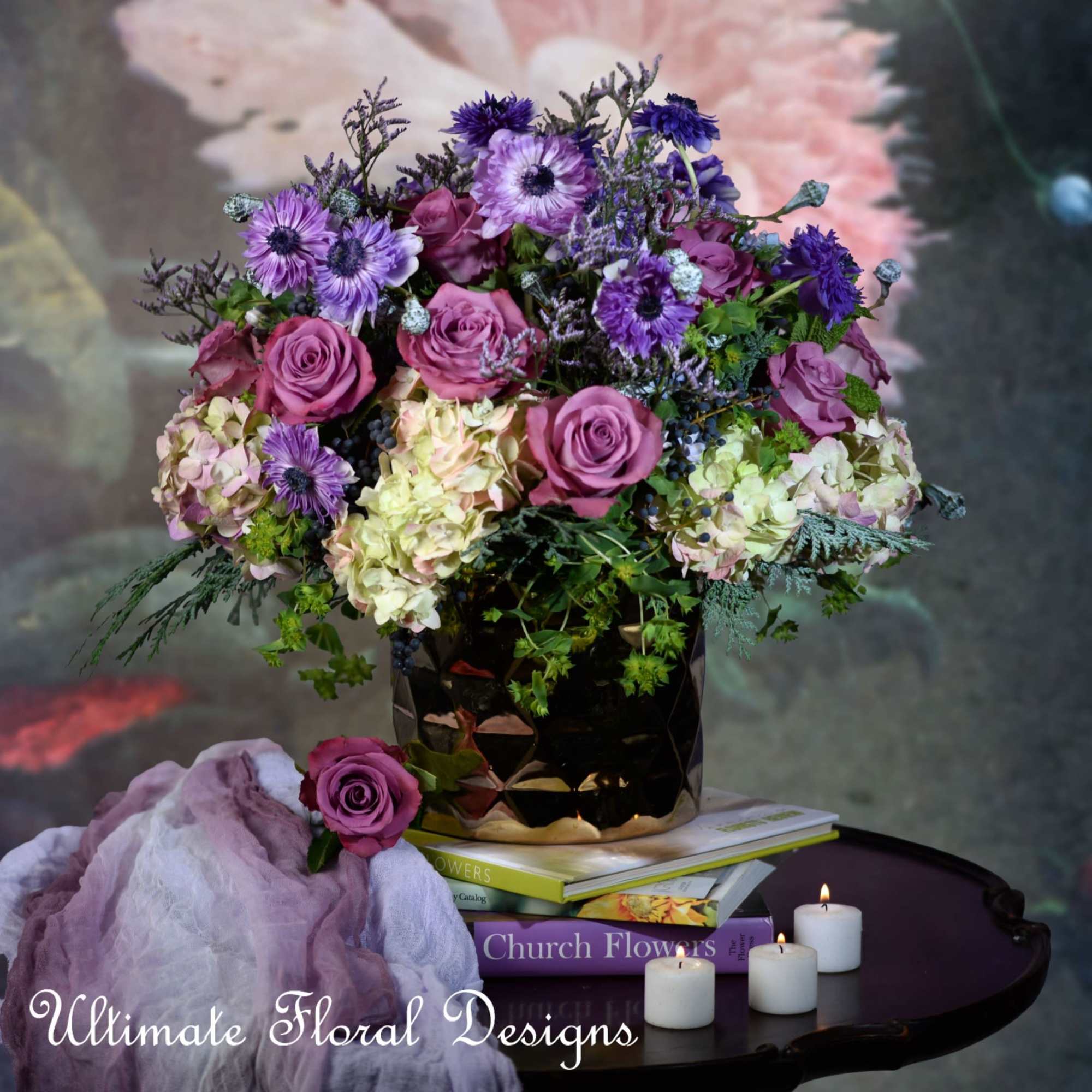 Purple and pink flower arrangement in a black vase with candles nearby