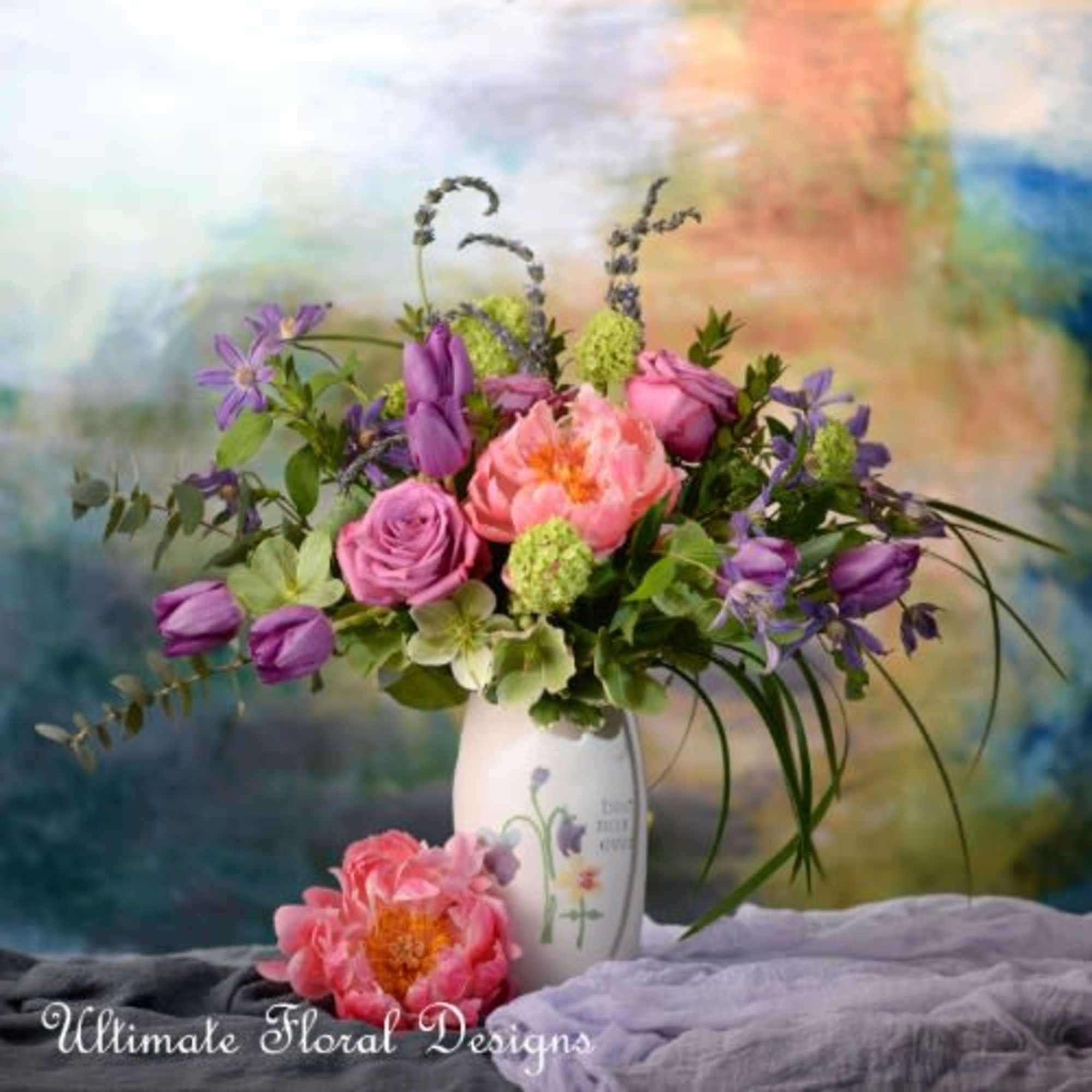 Pink and purple mixed bouquet in a white vase with two loose blooms in front