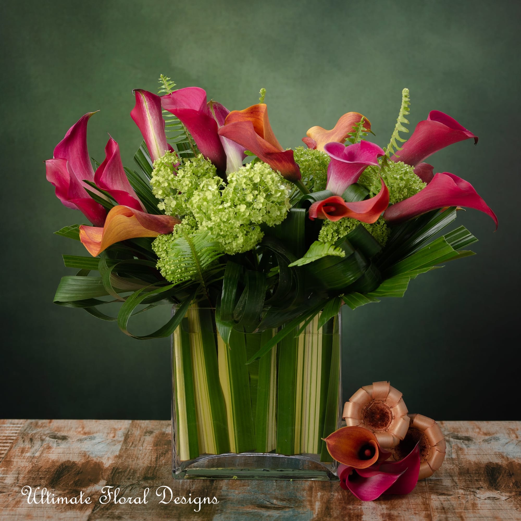 Modern arrangement of pink and orange calla lilies with green blooms in a leaf-lined glass cube vase