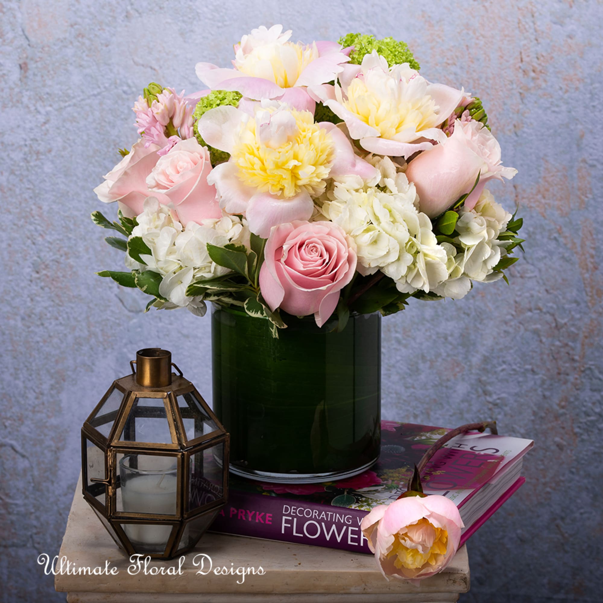 Pink and white flower arrangement in a dark green vase with a lantern beside it