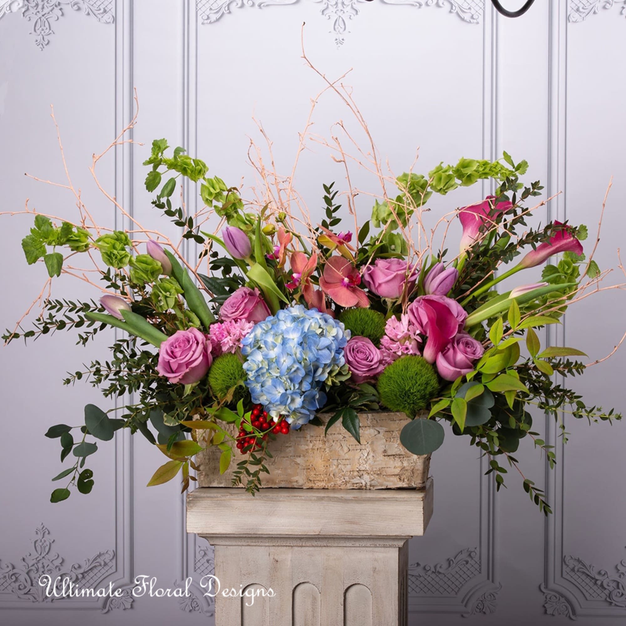Large floral arrangement with pink roses, blue hydrangea, and calla lilies in a stone container