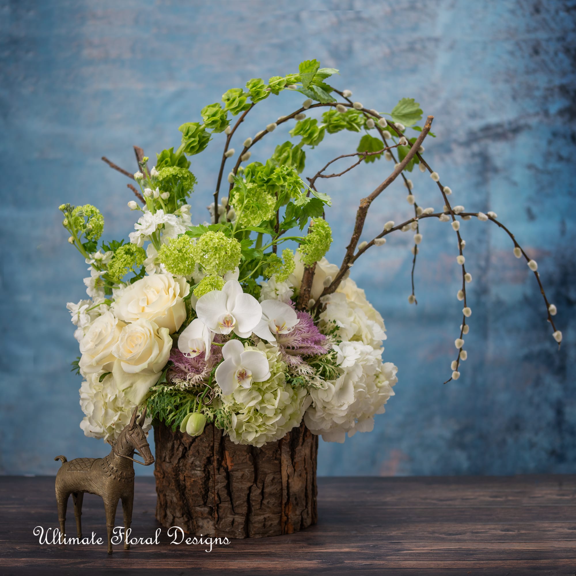 White and green floral arrangement in a rustic wood container with arched branches
