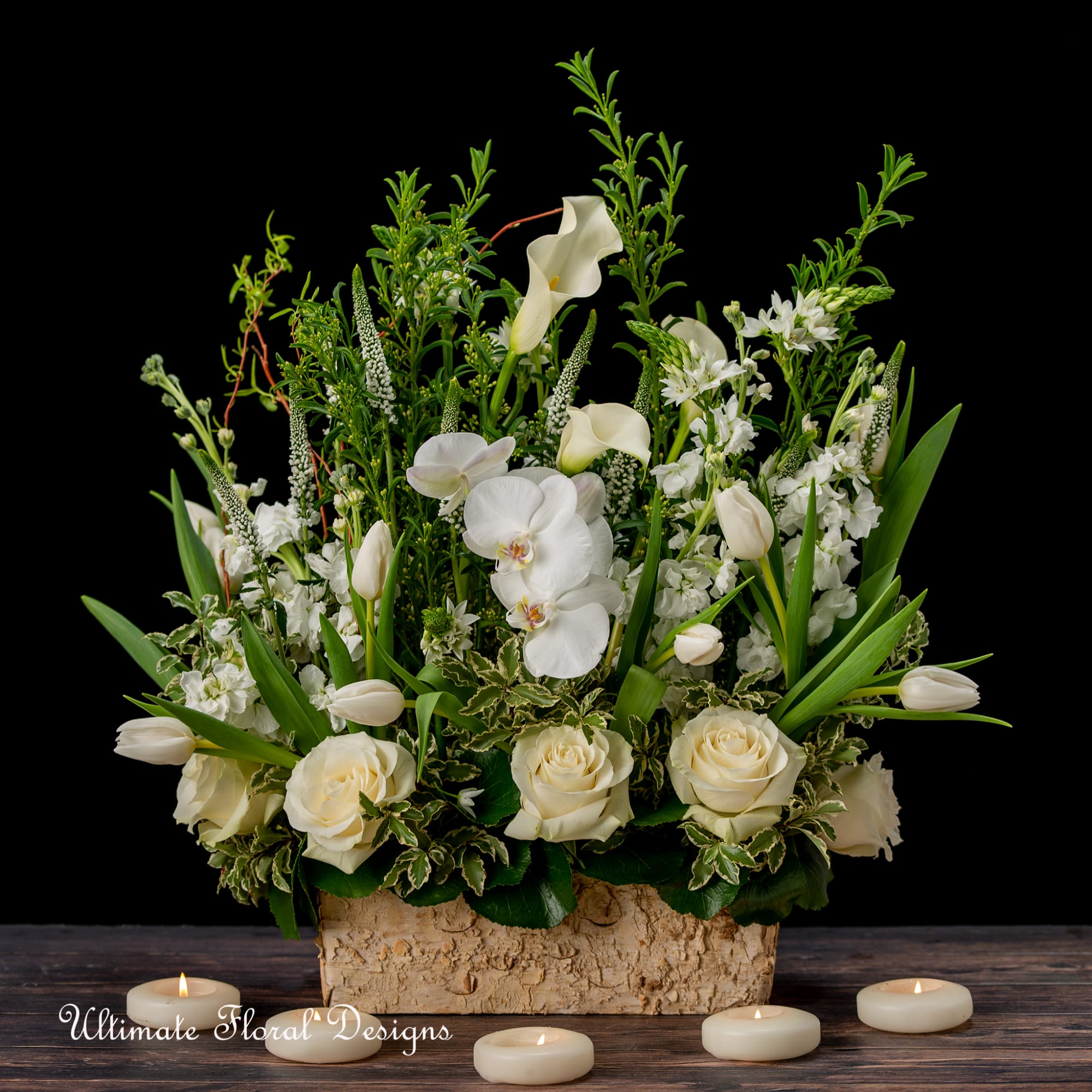 White floral arrangement with roses, orchids, and calla lilies in a bark container