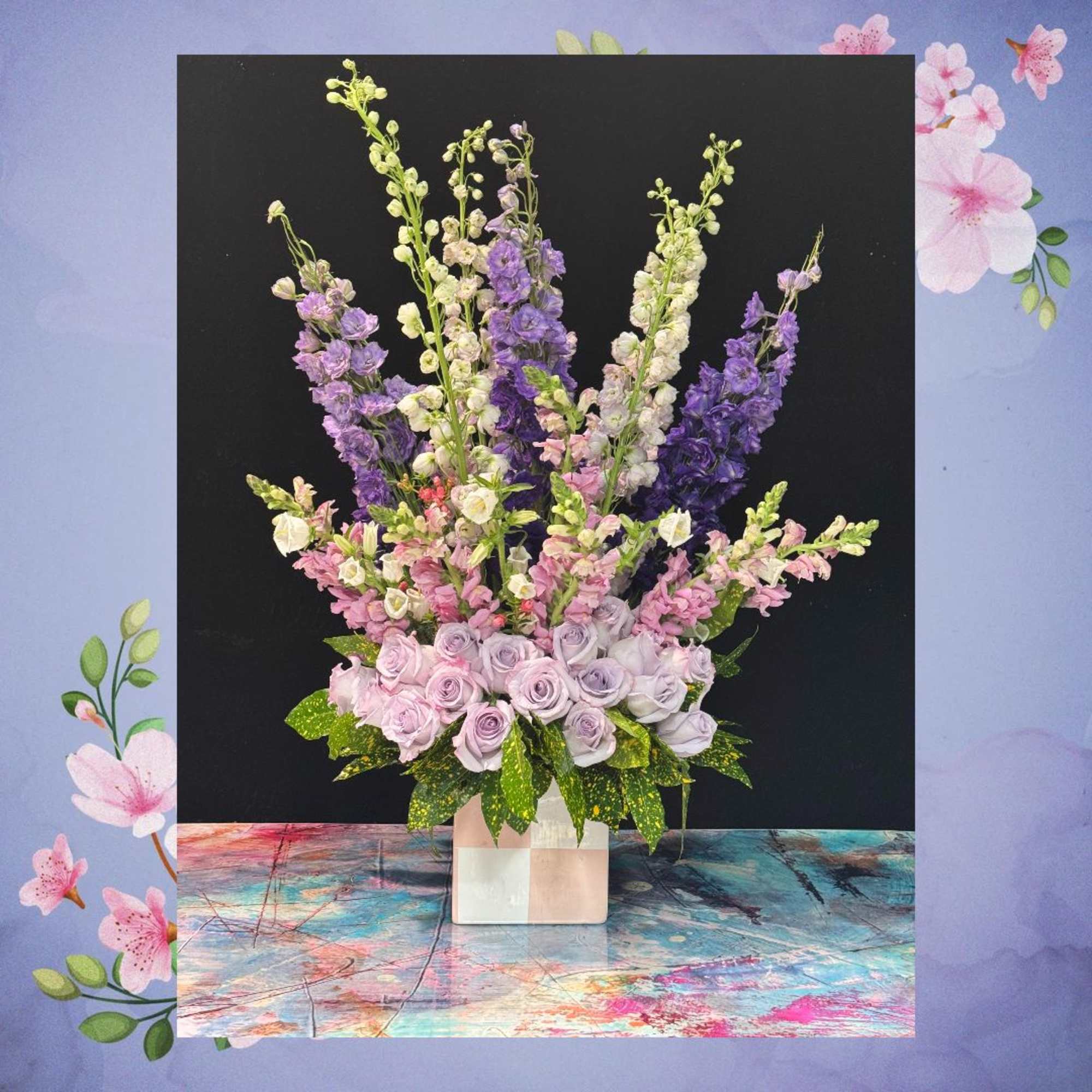 Tall arrangement of lavender and white flowers in a square vase