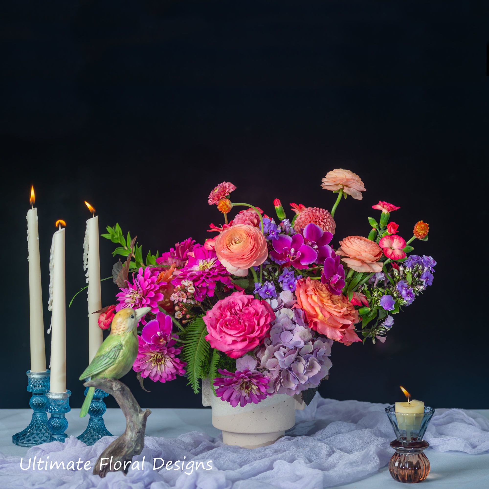 Colorful flower arrangement in a white vase with candles and a bird figurine