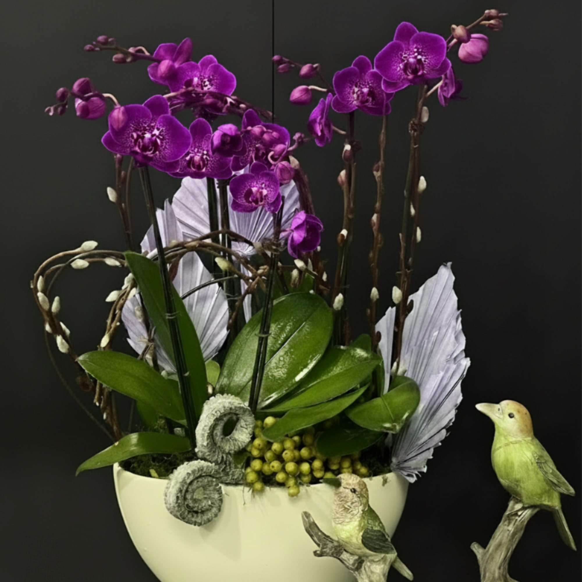 Purple orchids arranged in a white bowl with decorative bird figurines