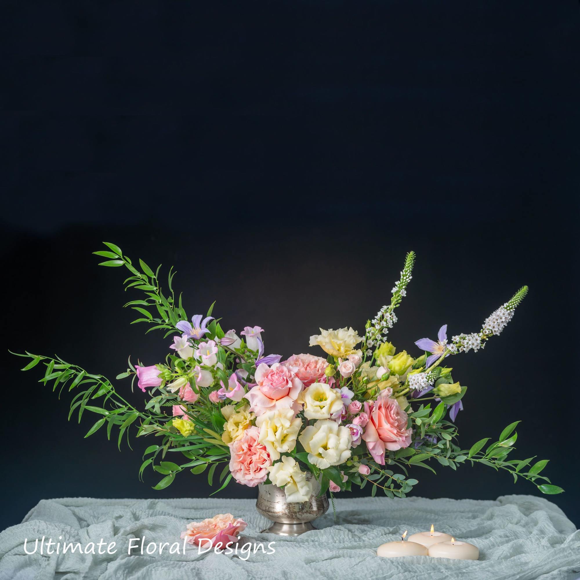Pastel floral arrangement in a silver vase with candles nearby
