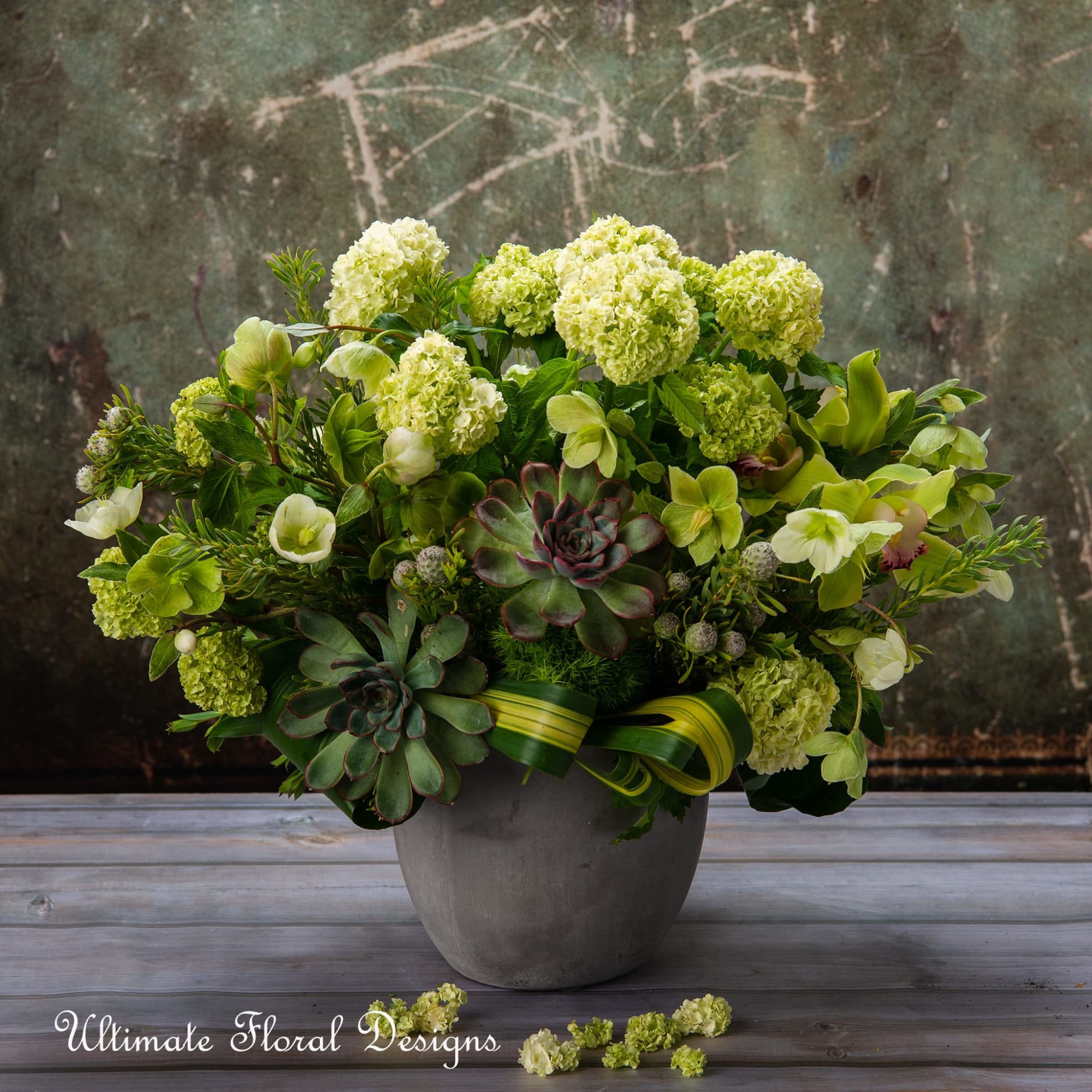 Green floral arrangement in a gray vase with succulents and pale blooms