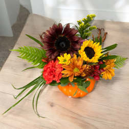 Autumn floral arrangement in an orange pumpkin container with sunflowers and carnations
