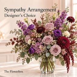Mixed purple and pink flowers in a clear glass vase with sympathy text.