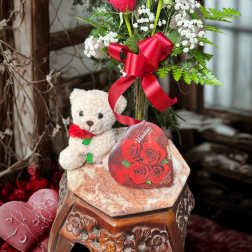 Red roses in a glass vase with a teddy bear and red ribbon