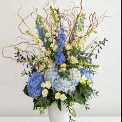 Tall blue and white floral arrangement in a white vase with curly branches