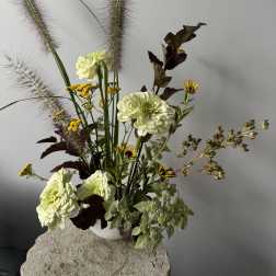 Tall floral arrangement with pale green blooms and feathery grasses in a white vase