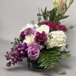 Mixed bouquet of roses, lilies, hydrangea, and purple flowers in a low vase