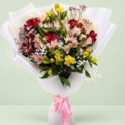 Mixed bouquet of pink, red, and yellow flowers wrapped in white paper with a pink ribbon