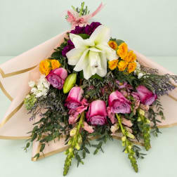 Bouquet of white lilies, pink roses, and yellow spray roses in pale wrapping