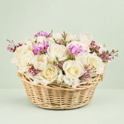 White roses and purple blooms arranged in a wicker basket