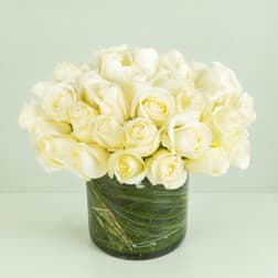 White roses arranged in a clear glass vase with green stems visible inside