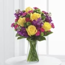 Bouquet of yellow roses and purple flowers in a clear glass vase