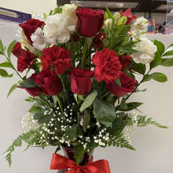 Tall arrangement of red roses and carnations with white blooms in a red vase with a red bow
