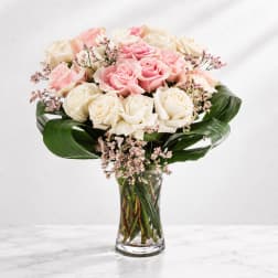 Pink and white roses in a clear glass vase with broad green leaves