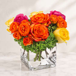 Bouquet of orange, yellow, and pink roses in a clear square vase