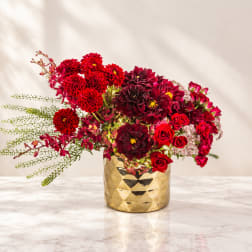 Red flowers arranged in a gold vase on a marble surface