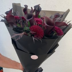 Bouquet of dark purple calla lilies and burgundy chrysanthemums in black wrap
