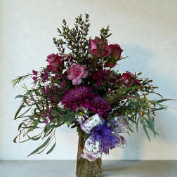 Purple and pink flower arrangement in a glass vase with a ribbon