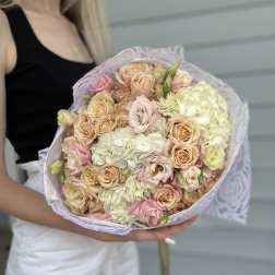 Handheld bouquet of blush roses and pale hydrangeas wrapped in lavender paper