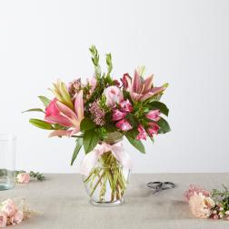 Pink lilies and roses arranged in a clear glass vase with a ribbon