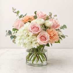 Pink roses, white hydrangea, and peach carnations in a clear glass vase