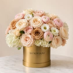 Pastel roses and ranunculus arranged in a gold hatbox