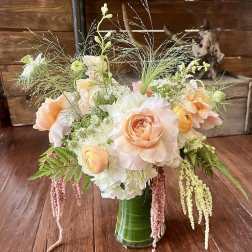 Peach roses and white blooms in a green glass vase