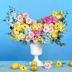 Colorful mixed bouquet in a white pedestal vase with lemons on the table