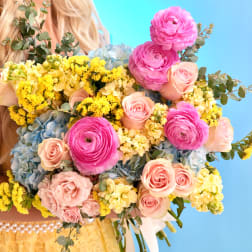 Large bouquet of pink, yellow, and blue flowers held in front of a person