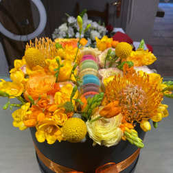 Orange and yellow floral arrangement in a black hatbox with ribbon