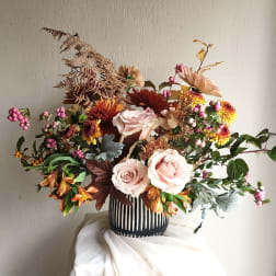 Mixed bouquet of pale pink roses and autumn-toned flowers in a striped vase
