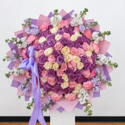 Heart-shaped bouquet of pink, purple, and cream roses with a lavender ribbon